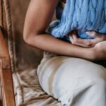 Woman sitting indoors holding a pillow against her stomach in discomfort