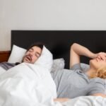 Man sleeping beside a woman who is covering her face due to his snoring