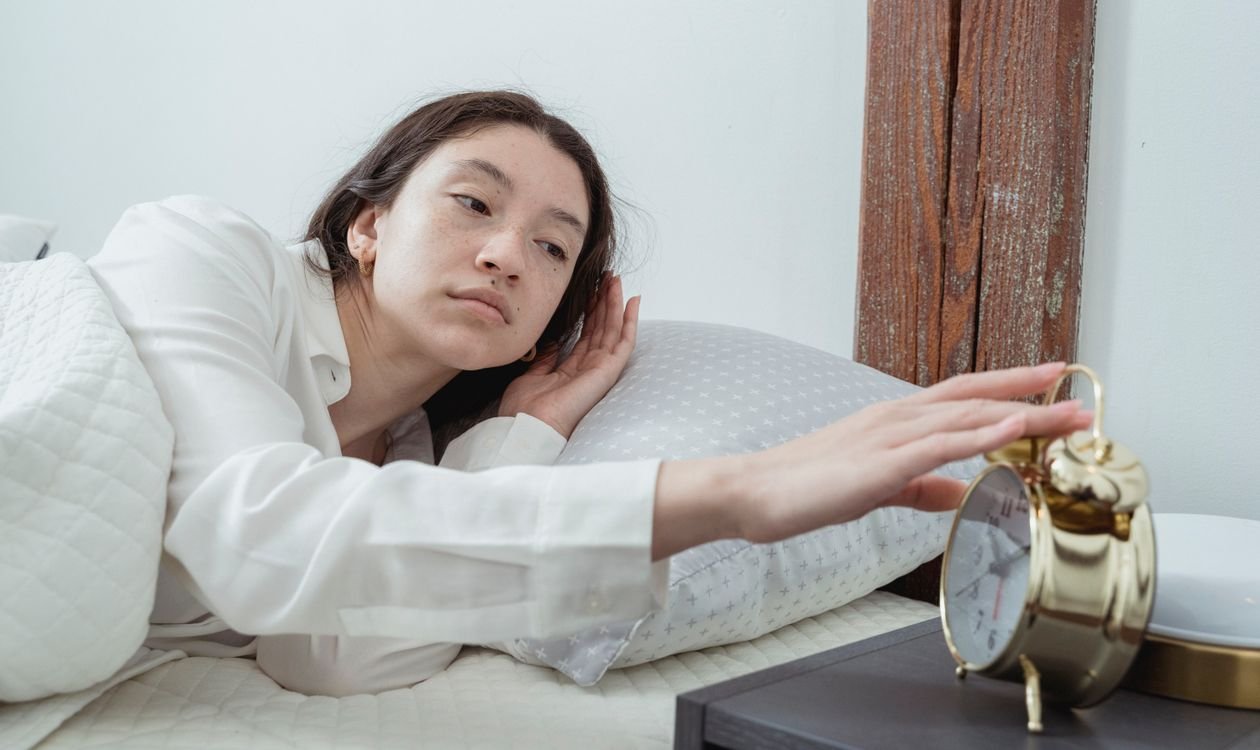 Woman waking up in bed and reaching for an alarm clock