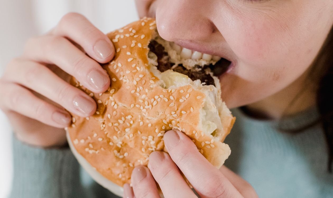 Woman taking a big bite of a burger, illustrating hunger